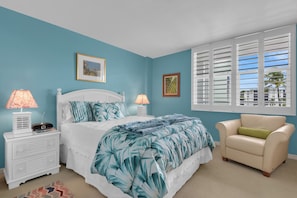 A bedroom with a bed, two bedside tables, a chair, and a window with shutters. - Beachfront Escape in the Moorings | Gulf Views & Coastal Breeze (Naples)