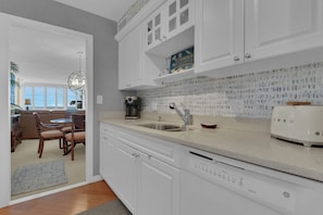 A kitchen with white cabinets, a coffee maker, a toaster, and a patterned backsplash. - Beachfront Escape in the Moorings | Gulf Views & Coastal Breeze (Naples)