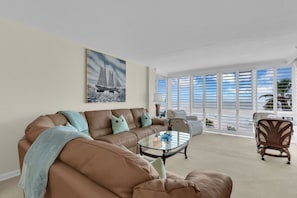 A living room with a brown leather sofa, a glass coffee table, and a view of the ocean through large windows. - Beachfront Escape in the Moorings | Gulf Views & Coastal Breeze (Naples)