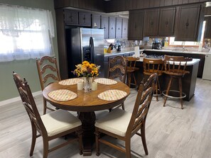 A kitchen with dark wooden cabinets, a stainless steel refrigerator, and a dining area with a round wooden table and chairs.