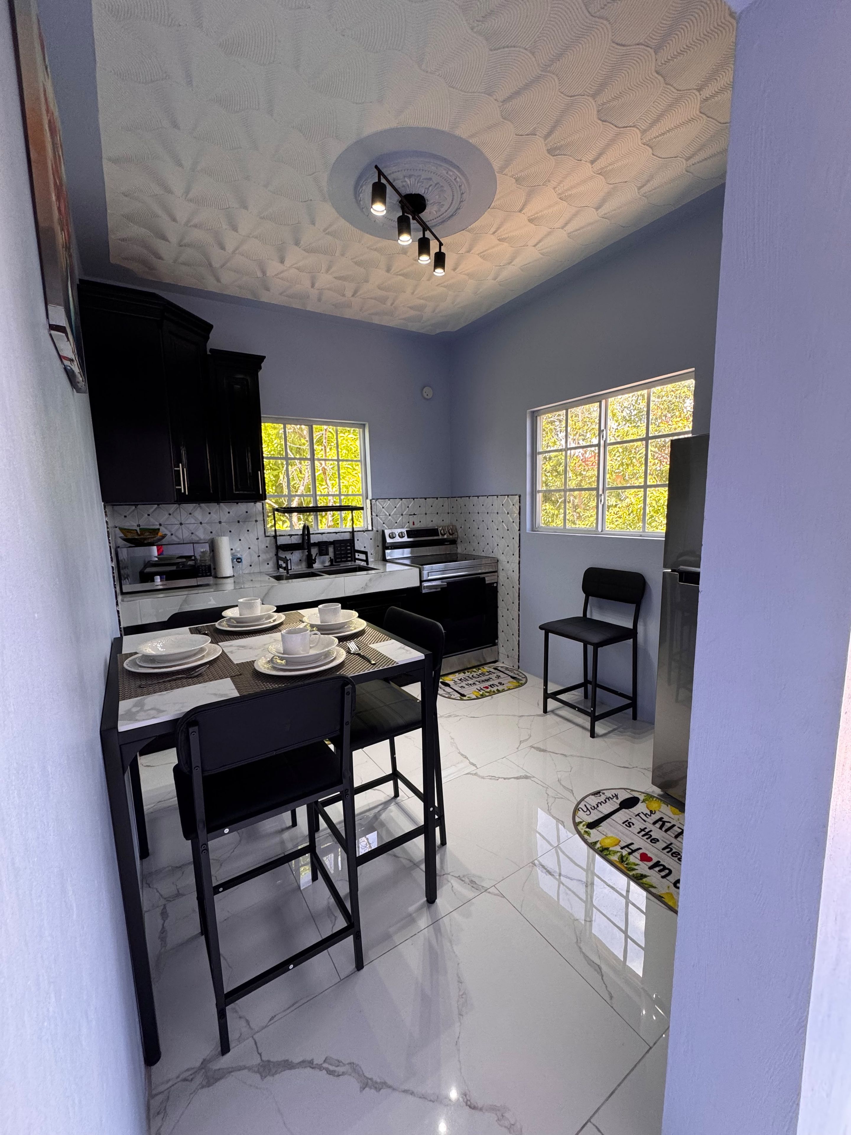 A modern kitchen with a dining area, featuring a marble countertop, black chairs, and a built-in oven.