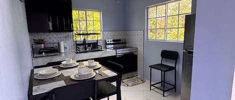A modern kitchen with a dining area, featuring a marble countertop, black chairs, and a built-in oven.