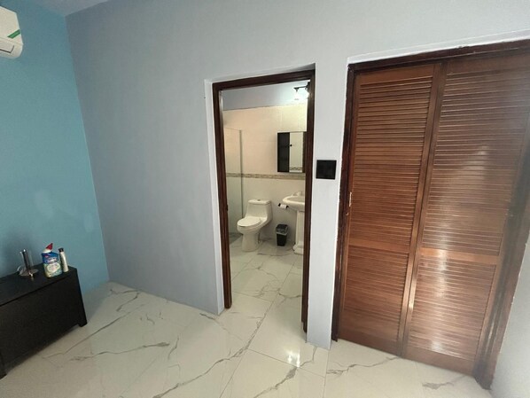 Ein Flur, der zu einem Badezimmer mit Toilette, Waschbecken und Spiegel führt.