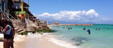 A beach with clear water, people swimming, and buildings in the background.