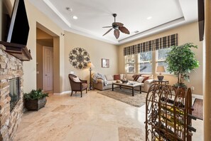 A spacious living room with a stone fireplace, a ceiling fan, and a large window with blinds. - 2 bed, 2.5 bath Oasis: Clubhouse, Pool, Gym- Steps to Polo Concerts Golf Tennis! (La Quinta)