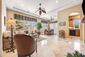 A spacious living area with a ceiling fan, a dining table with chairs, a sofa, and a kitchen area with cabinets and a dishwasher. - 2 bed, 2.5 bath Oasis: Clubhouse, Pool, Gym- Steps to Polo Concerts Golf Tennis! (La Quinta)