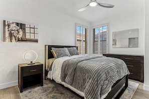 A bedroom with a bed, bedside tables, a ceiling fan, a window with blinds, a mirror, and a painting on the wall. - Remodeled 3BR Kierland | Garage, Pool, Spa, Golf (Scottsdale)