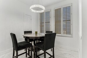 A dining area with a round table, four chairs, a chandelier, and a window with shutters. - Remodeled 3BR Kierland | Garage, Pool, Spa, Golf (Scottsdale)