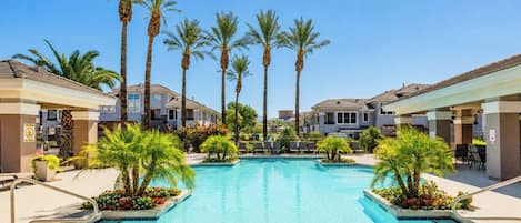 A swimming pool with palm trees, lounge chairs, and a clear blue sky.