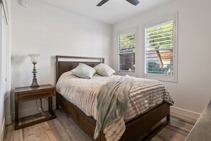 A bedroom with a bed, bedside table, lamp, and window with blinds. - Black & Gold Luxe | No Stairs | Pool & Spa (Scottsdale)