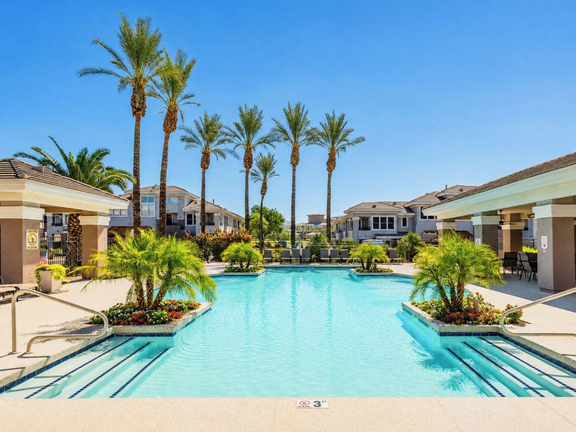A swimming pool with palm trees, lounge chairs, and a clear blue sky.