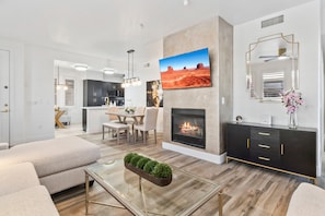 A modern living room with a fireplace, a dining area, and a kitchen in the background. - Black & Gold Luxe | No Stairs | Pool & Spa (Scottsdale)