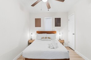 Ein Schlafzimmer mit einem Bett, zwei Nachttischen, einem Deckenventilator und einer Tür.