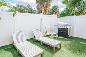 Ein Garten mit zwei Liegestühlen, einem Grill und einem weißen Zaun.