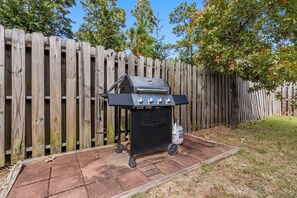 Een barbecue met gasfles en propaancilinder, opgesteld tegen een houten schutting en een gazon.