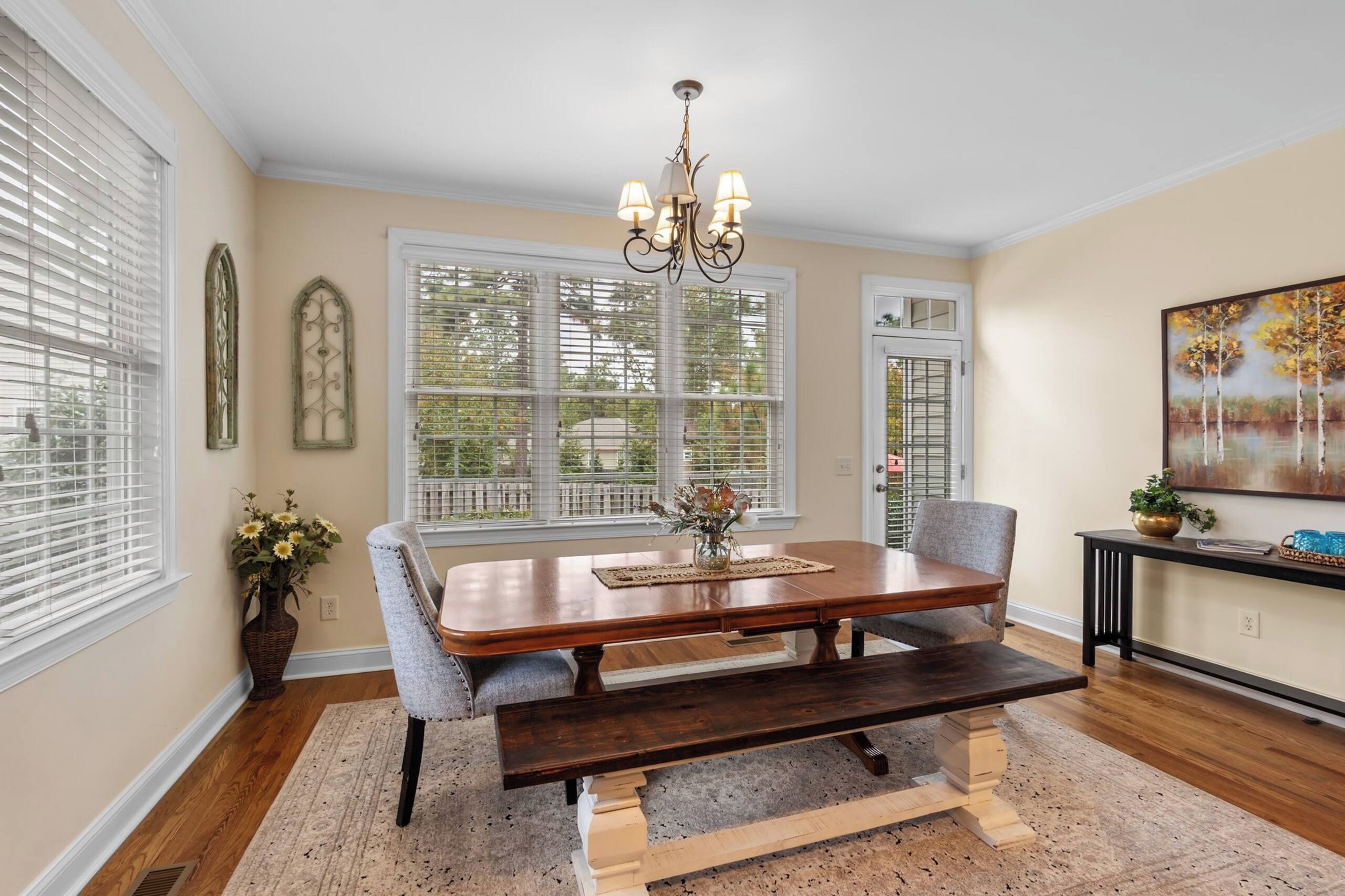 A dining room with a wooden table, chairs, a chandelier, and a painting on the wall.