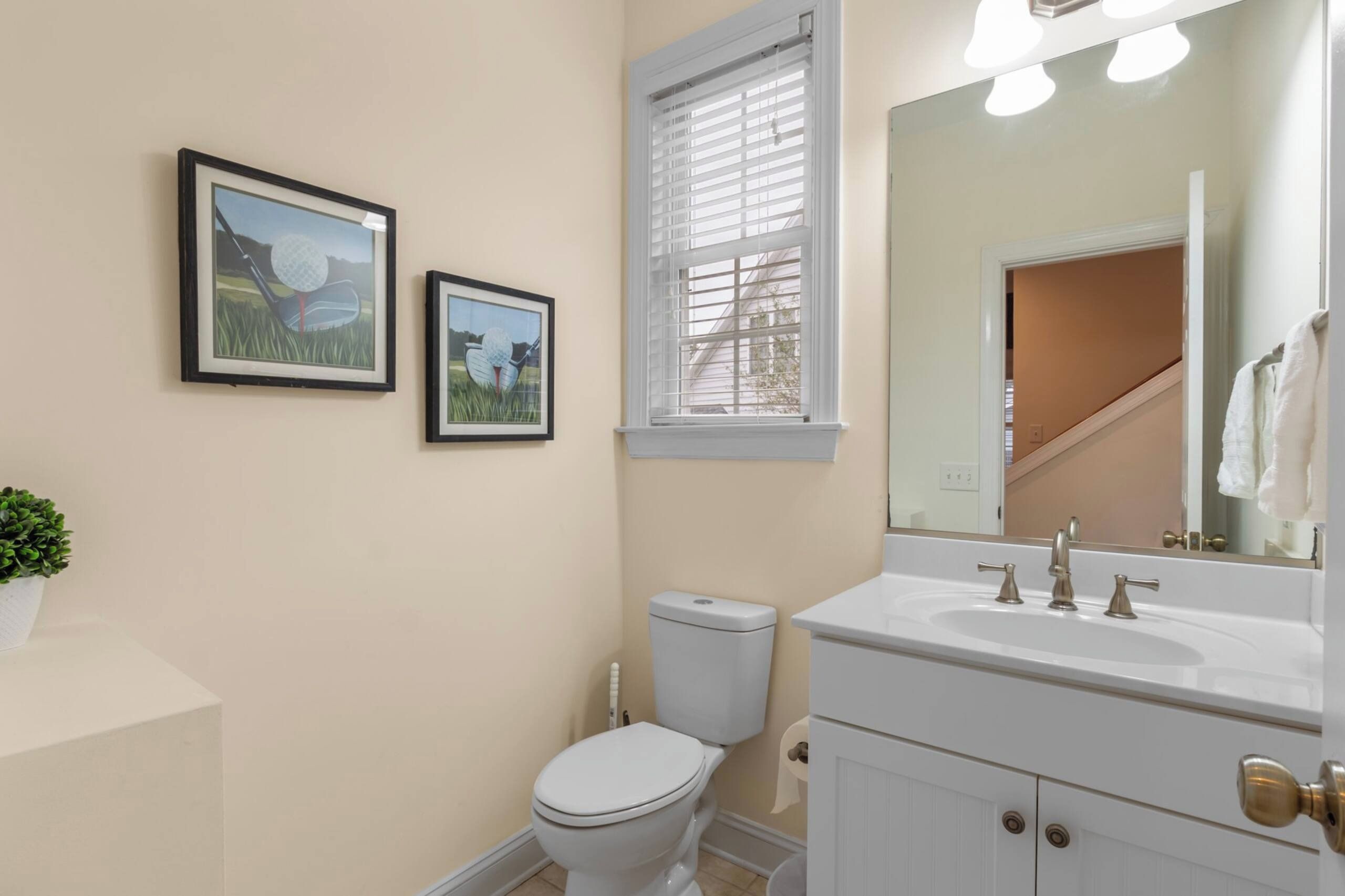 A bathroom with a toilet, sink, and two framed pictures on the wall.