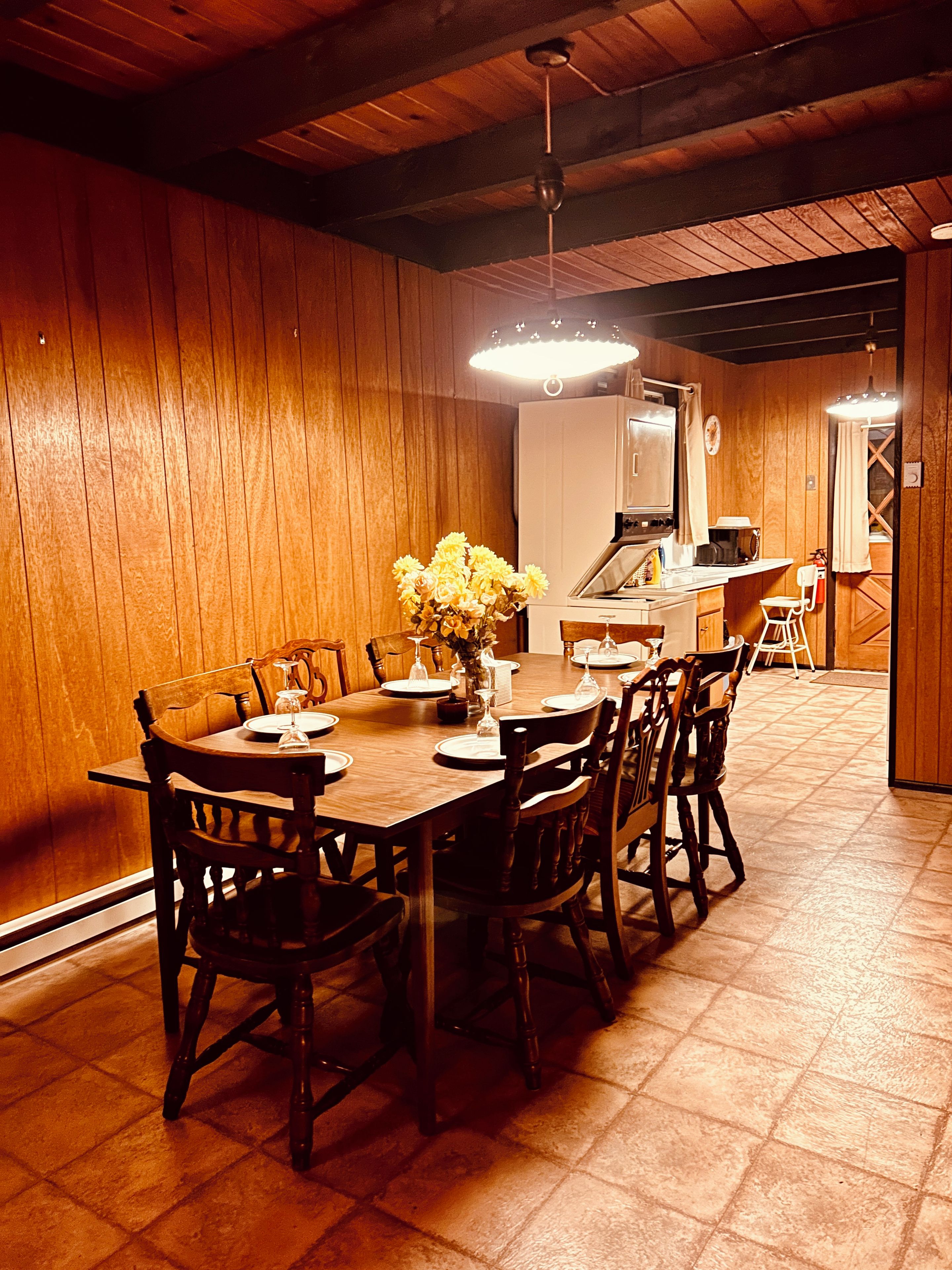 Una mesa de comedor de madera con sillas, un florero y una lámpara colgante.