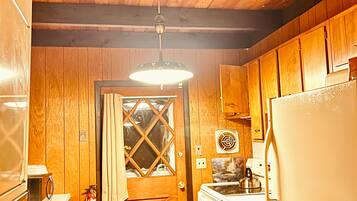 A compact kitchen with wooden cabinets, a refrigerator, a stove, and a hanging light fixture.