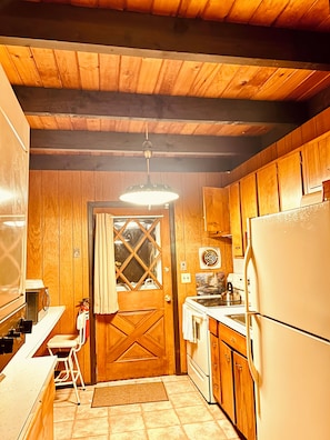 A compact kitchen with wooden cabinets, a refrigerator, a stove, and a hanging light fixture.
