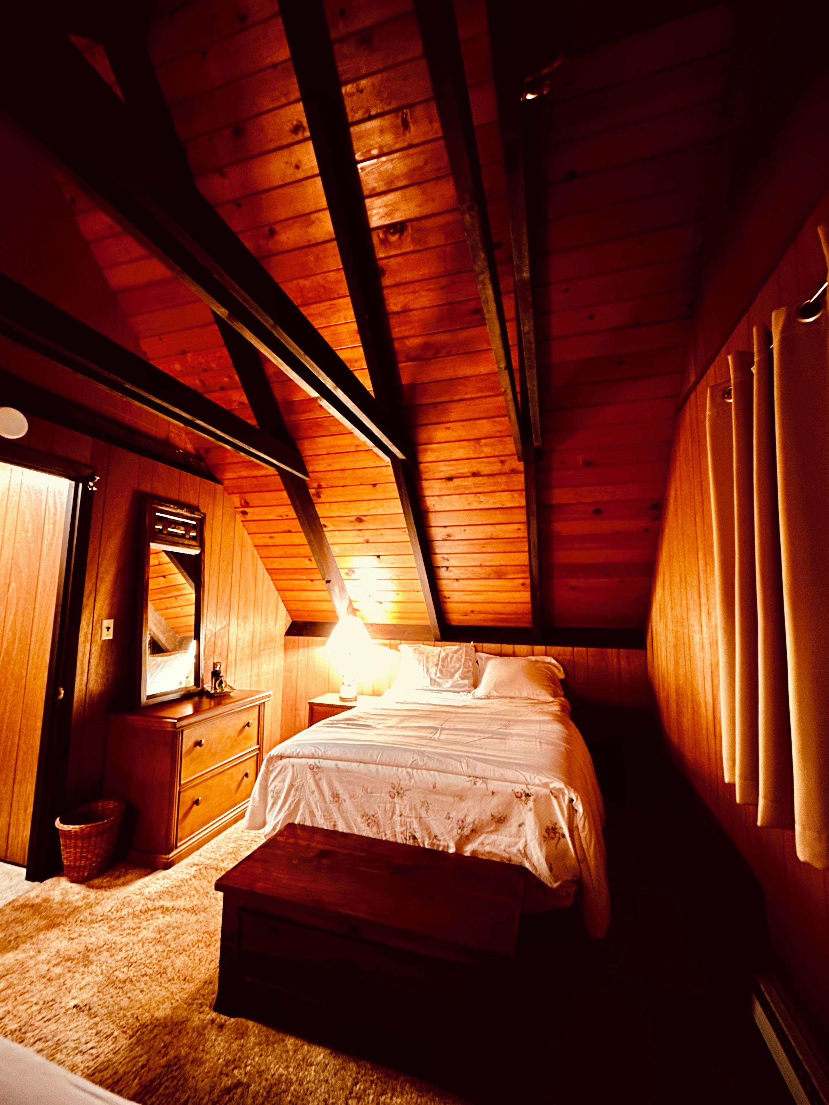 A bedroom with a wooden ceiling, a bed, a dresser, and a mirror.