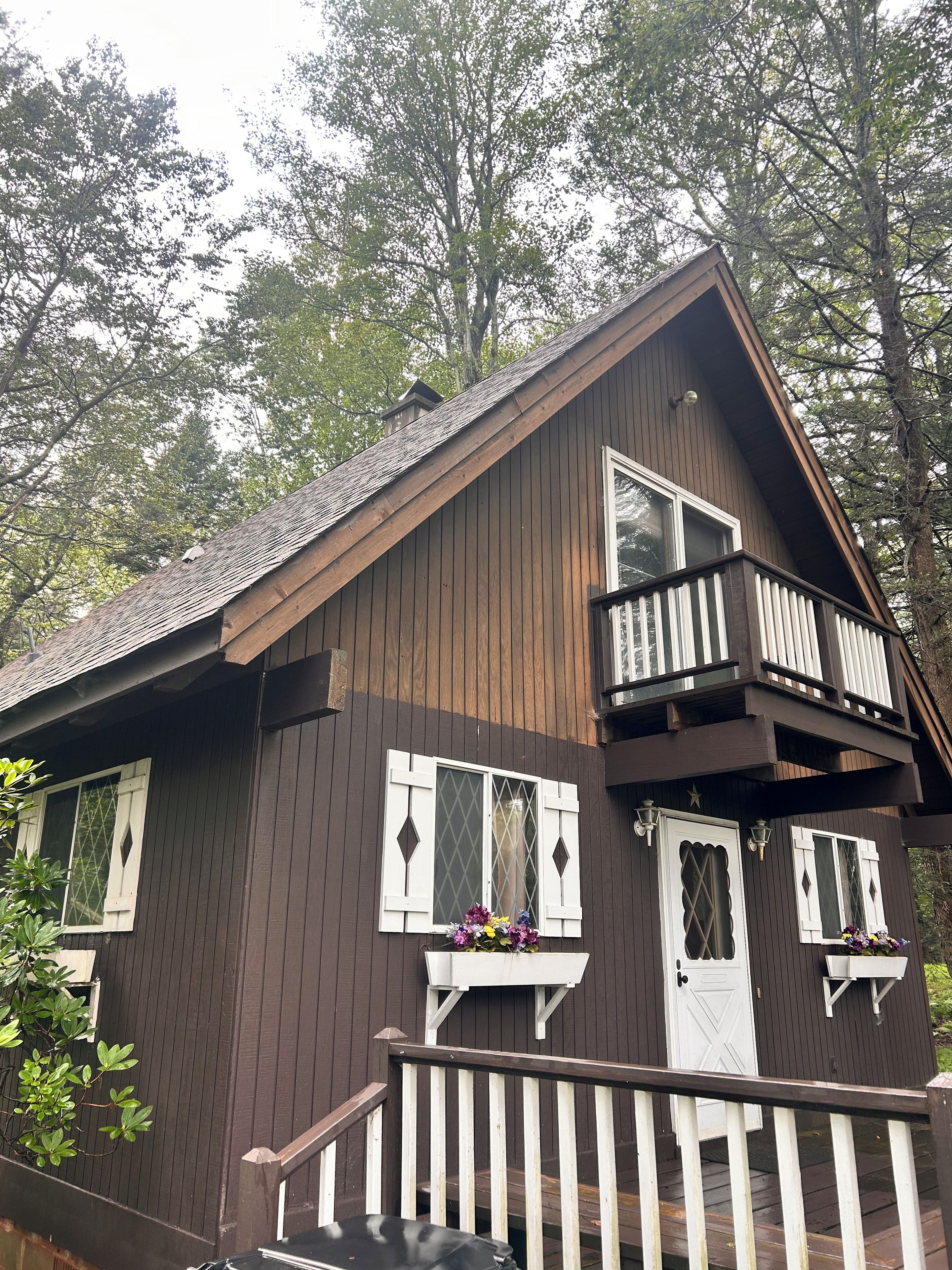 A two-story wooden cabin with a balcony, white shutters, and a deck.