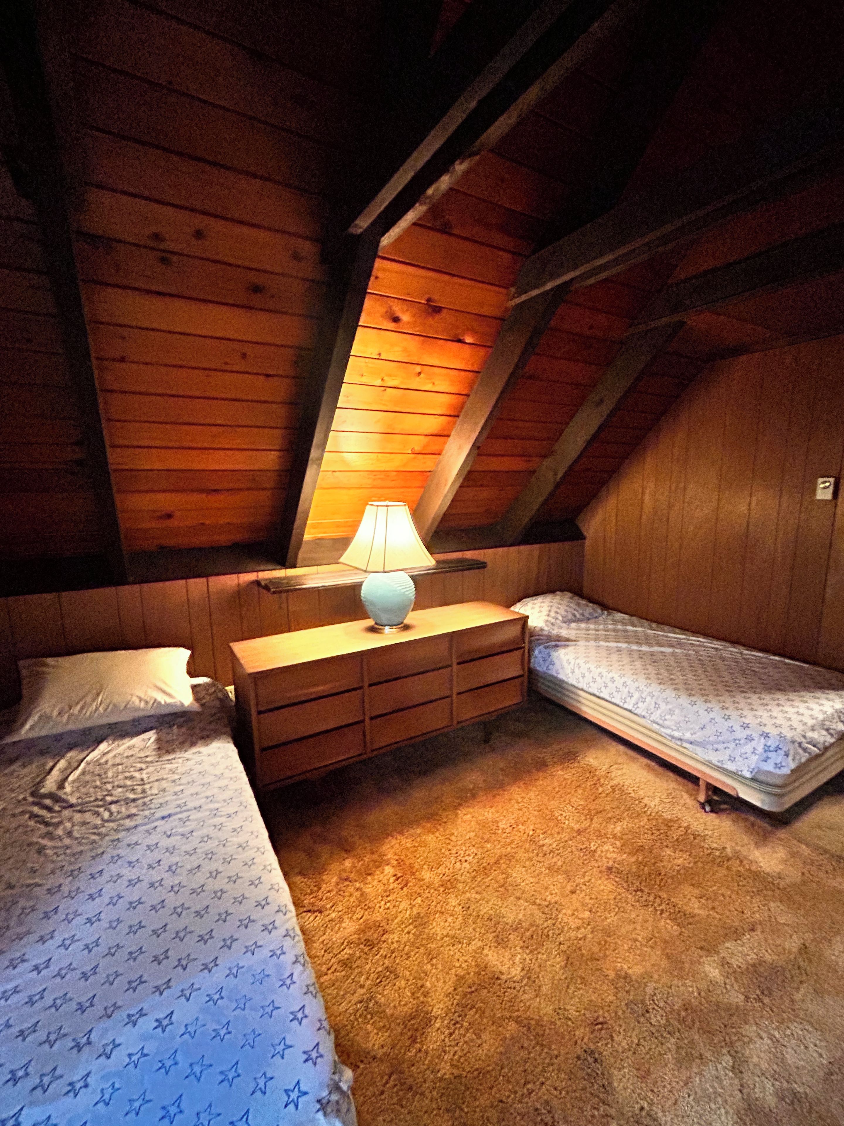 A bedroom with two beds, a nightstand, and a lamp.