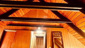 A wooden interior with a sloped ceiling, a hallway leading to a bathroom, and a dresser with a mirror.