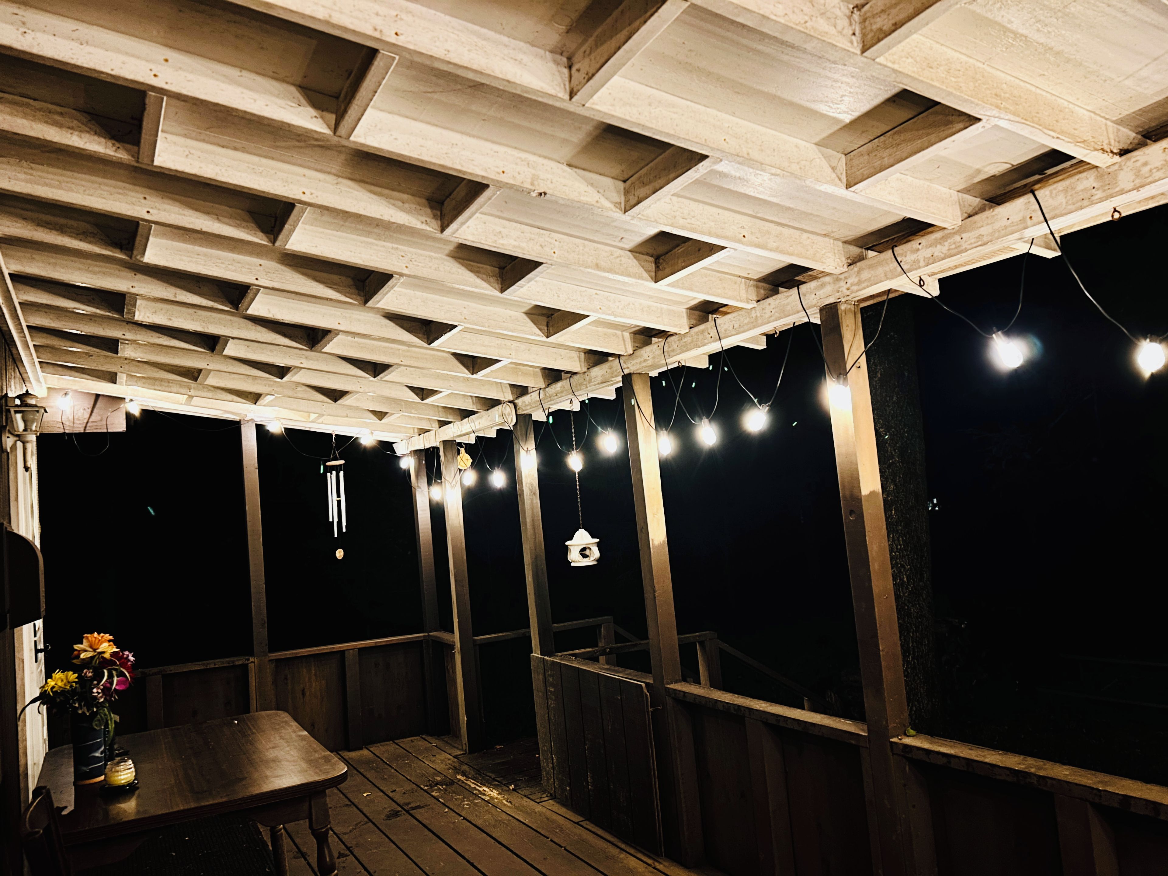 En träaltan med ett bord och stolar, ljusslingor och en hängande lampa.