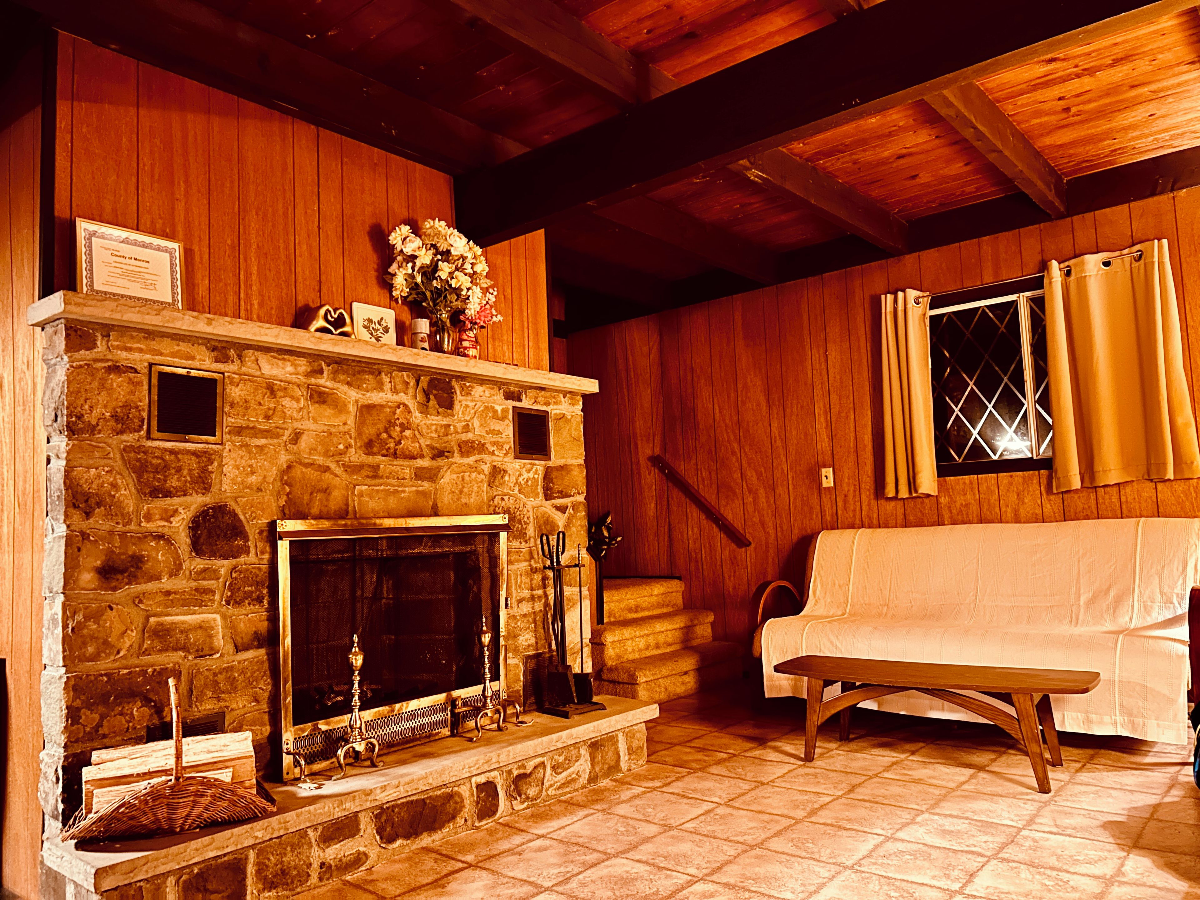 A stone fireplace with a mantel, a wooden bench, and a window with curtains.