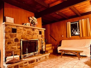 A stone fireplace with a mantel, a wooden bench, and a window with curtains.