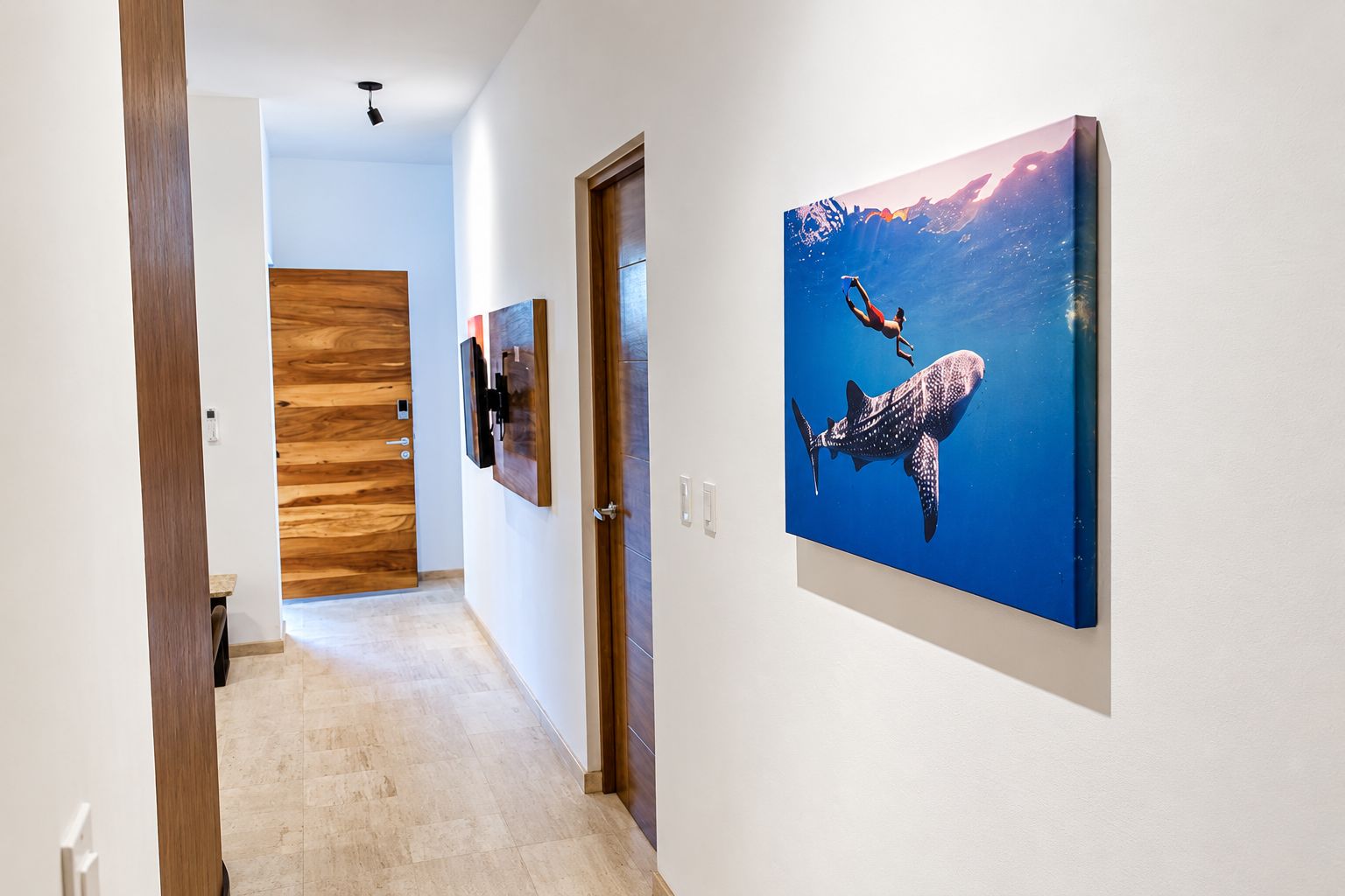 Un pasillo con una puerta de madera, un cuadro enmarcado de un tiburón ballena y un piso de baldosas.