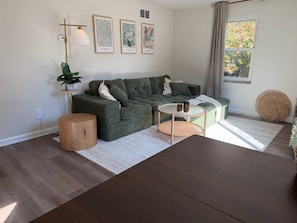 A living room with a sectional sofa, a coffee table, a round side table, and a potted plant. - Newly Furnished and Updated Apartment, Peaceful Neighbourhood (Euclid)