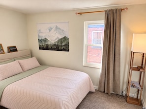 A bedroom with a bed, a window with curtains, a wall-mounted lamp, and a painting. - Newly Furnished and Updated Apartment, Peaceful Neighbourhood (Euclid)