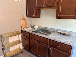 A kitchen with wooden cabinets, a granite countertop, a sink, and a small wooden cutting board. - Newly Furnished and Updated Apartment, Peaceful Neighbourhood (Euclid)