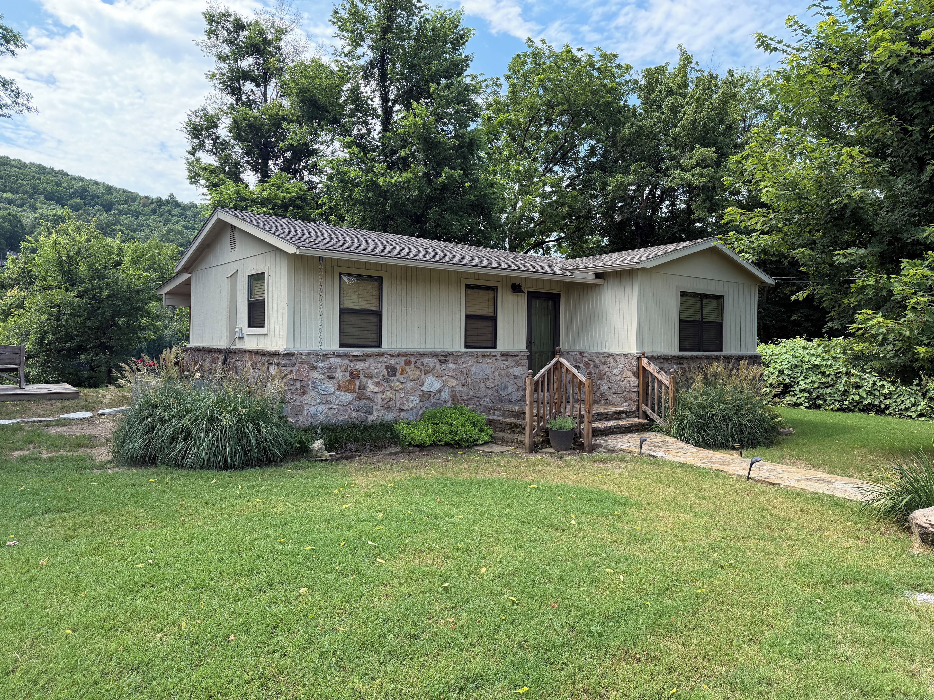 A two-story house with a stone foundation, a front porch with a wooden railing, and a well-maintained lawn.