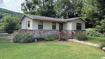 A two-story house with a stone foundation, a front porch with a wooden railing, and a well-maintained lawn.