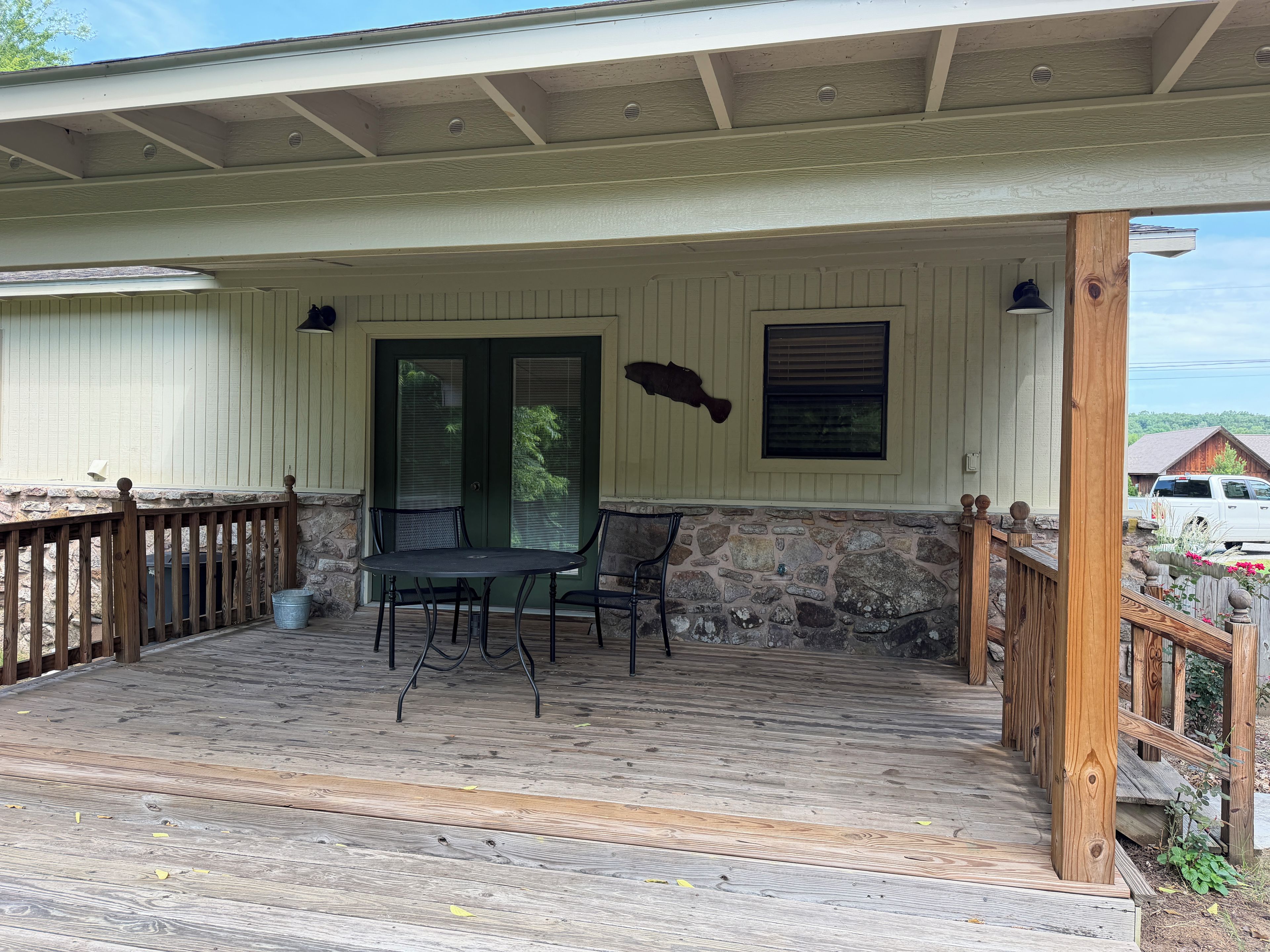 Un espace extérieur abrité, doté d’un mur en pierre, d’une terrasse en bois et d’une table avec des chaises.