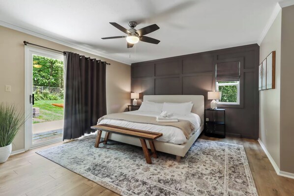 Ein Schlafzimmer mit Bett, Nachttischen, Deckenventilator und Blick auf Grünflächen.