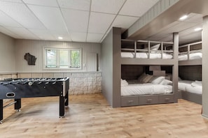 A room with a foosball table, bunk beds, and a window with blinds. - Hillside Haven | Beach Access, Game Room & Fire Pit (Lake Geneva)