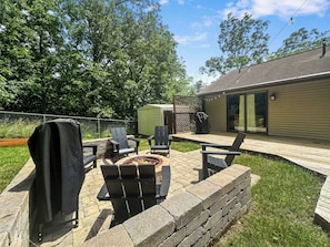 An outdoor patio with a fire pit, seating, and a covered grill area. - Hillside Haven | Beach Access, Game Room & Fire Pit (Lake Geneva)