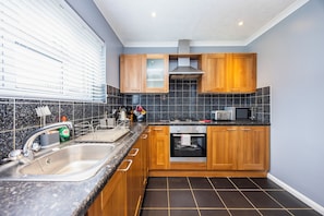 Een moderne keuken met granieten werkbladen, roestvrijstalen apparatuur en houten kastjes.