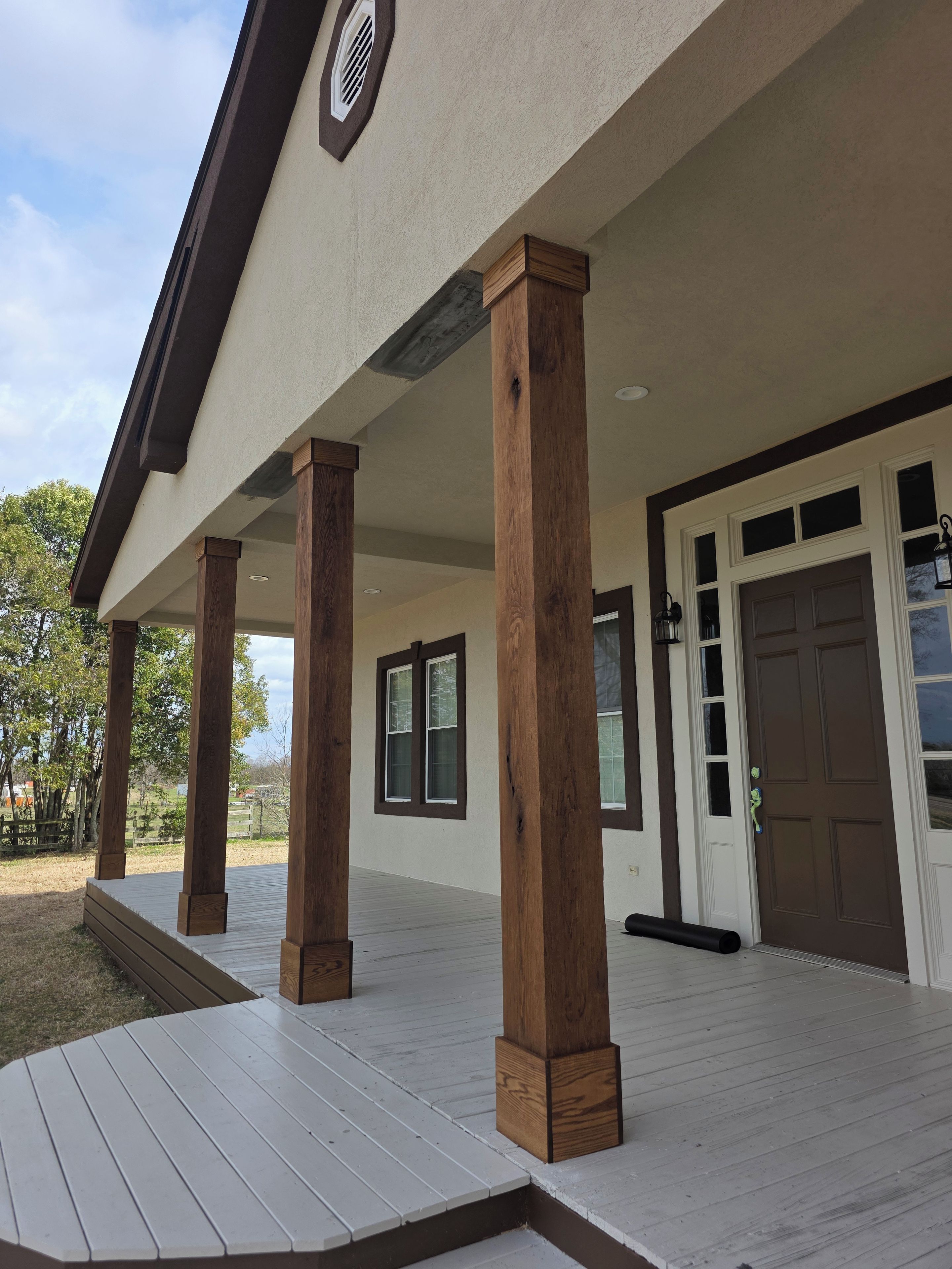 A covered outdoor area with wooden columns, a door, and windows.