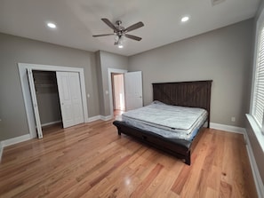 A bedroom with a wooden floor, a bed with a headboard, a ceiling fan, and two doors.