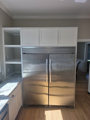 A stainless steel refrigerator in a kitchen with white cabinetry and a wooden floor.