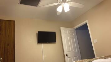 A bedroom with a ceiling fan, a mounted television, a door, and a bed with a patterned bedspread.