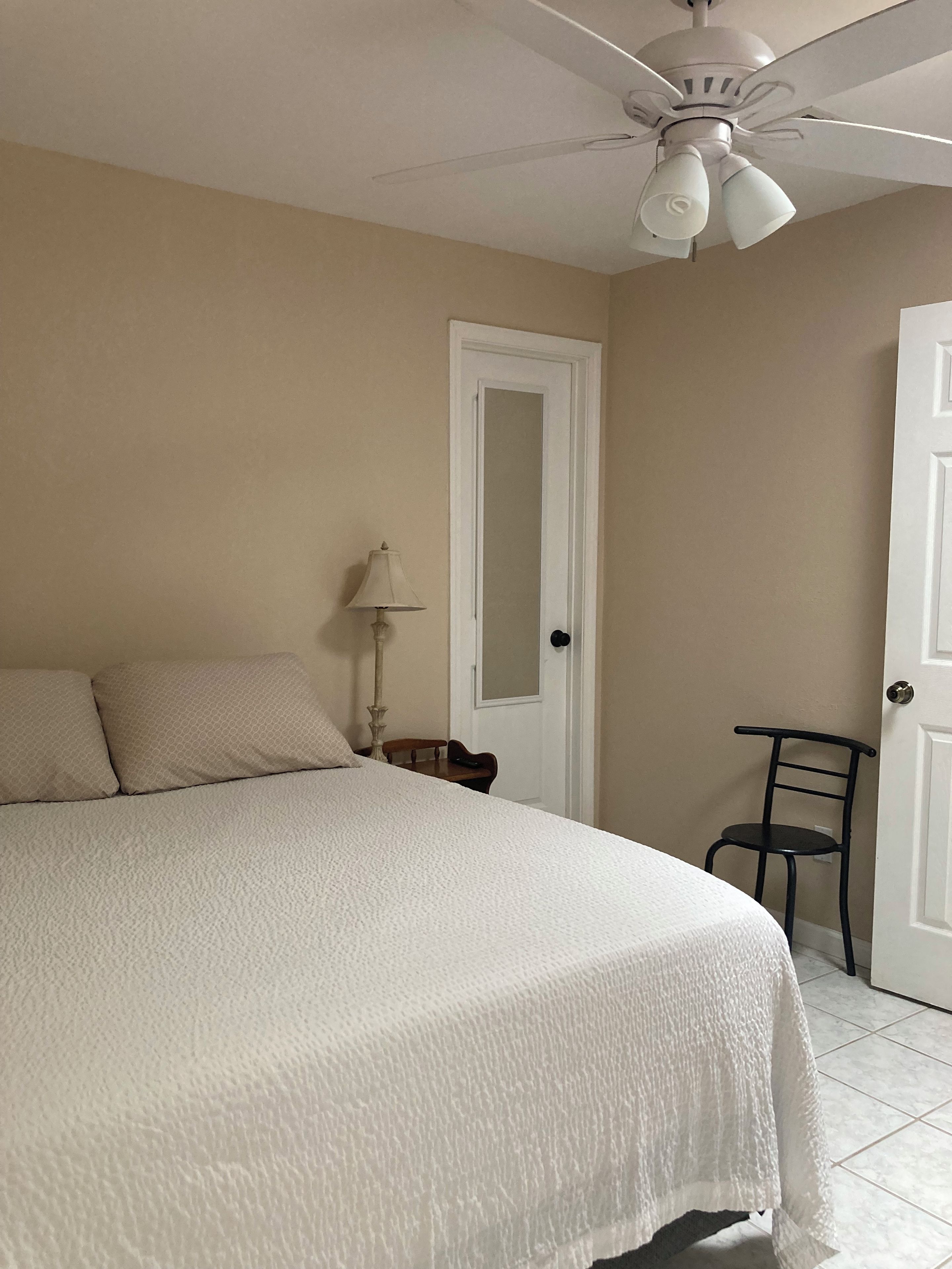 A bedroom with a bed, a ceiling fan, a door, and a chair.