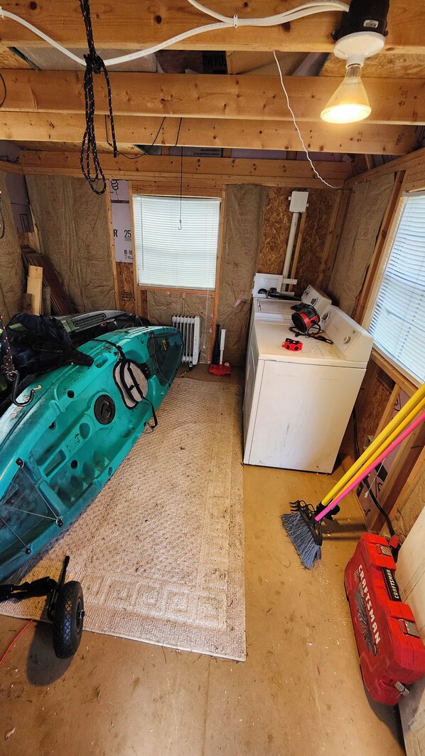 A room with a kayak, a washing machine, and a broom.