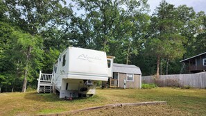 A recreational vehicle (RV) parked in a grassy area with a wooden deck and a small building in the background.