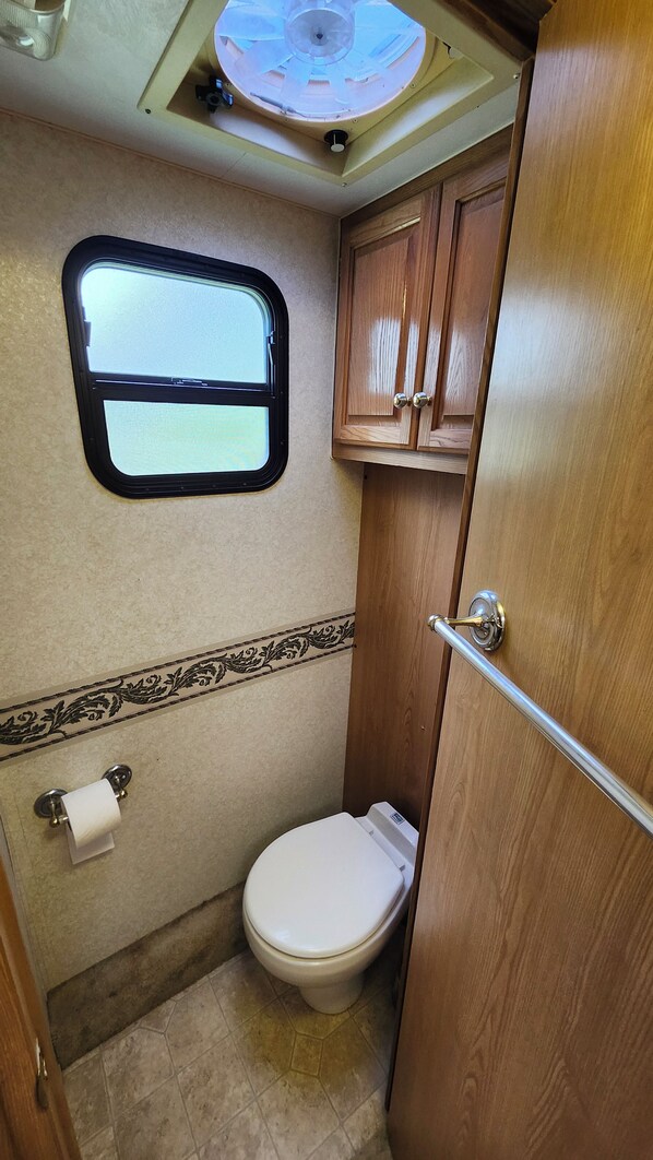 Baño de una caravana compacto, con inodoro, ventana y armarios de madera.